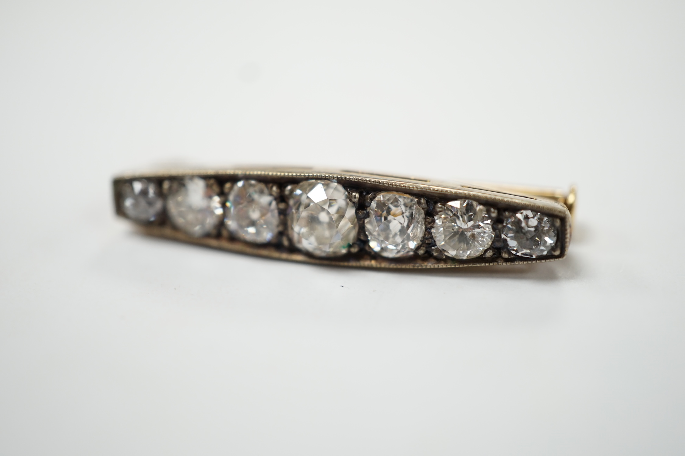 A small yellow metal and seven stone graduated diamond set bar brooch, 28mm, gross weight 3.9 grams (two cracks to one stone). Fair condition.